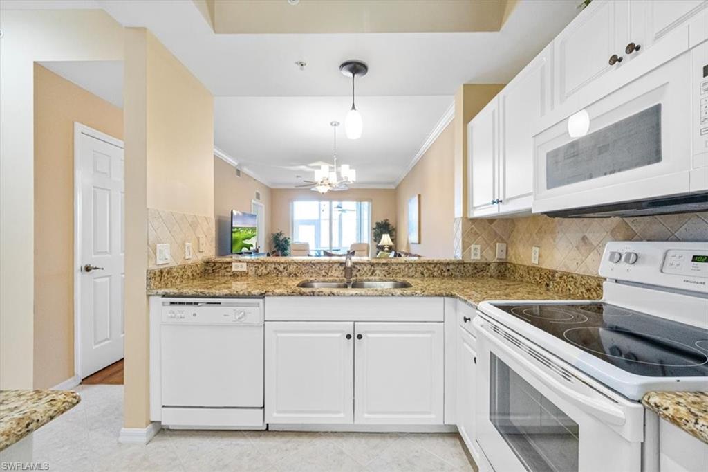 Kitchen with white appliances, backsplash, white cabinetry, light stone countertops, and decorative light fixtures