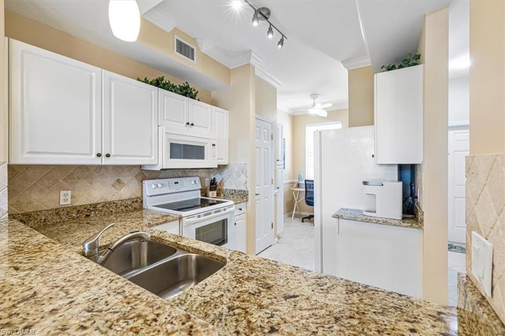 Kitchen with white cabinetry, white appliances, crown molding, decorative backsplash, and light stone counters