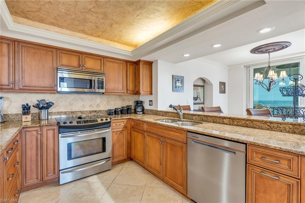 Kitchen with crown molding, sink, appliances with stainless steel finishes, a tray ceiling, and a notable chandelier / virtually enhanced image