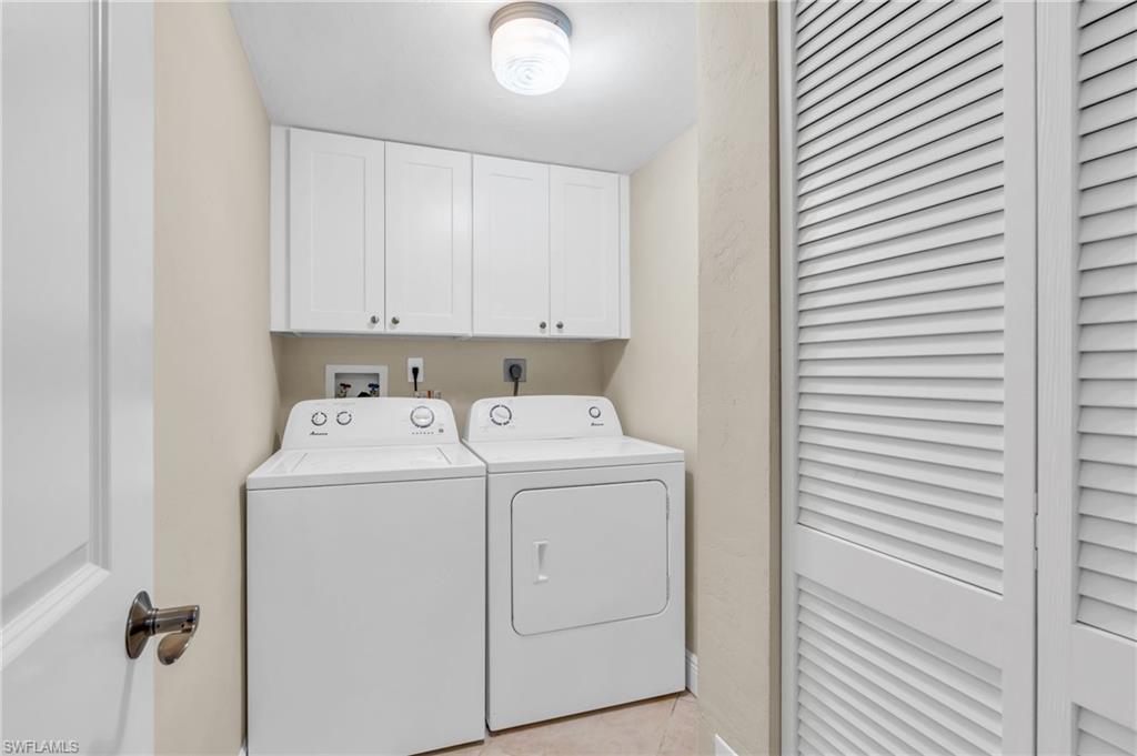 Clothes washing area featuring cabinets, light tile patterned floors, and washer and clothes dryer / virtually enhance image