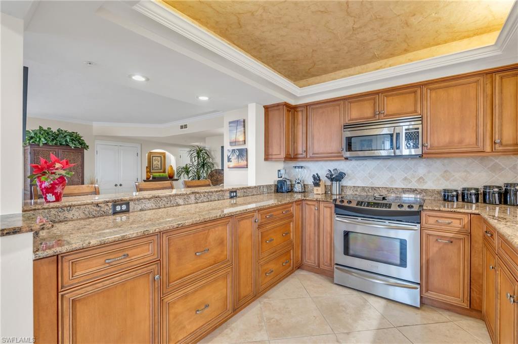 Kitchen featuring a raised ceiling, decorative backsplash, appliances with stainless steel finishes, light stone counters, and kitchen peninsula / virtually enhanced image
