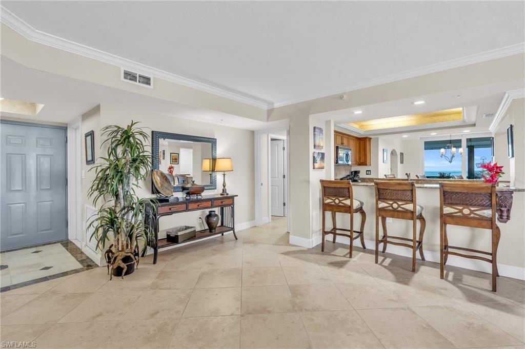 Kitchen with an inviting chandelier, a tray ceiling, light tile patterned flooring, kitchen peninsula, and a breakfast bar area / virtually enhanced image