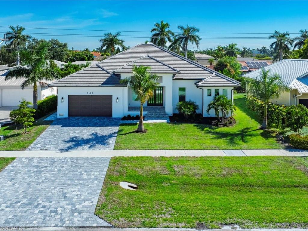 View of front of home with decorative driveway, a front yard, a garage, stucco siding, and a tiled roof
