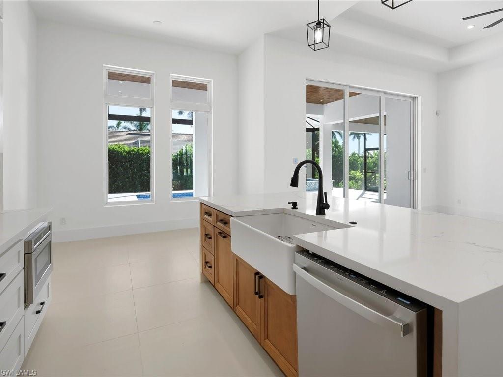 Kitchen featuring brown cabinetry, appliances with stainless steel finishes, a center island with sink, light stone counters, and recessed lighting