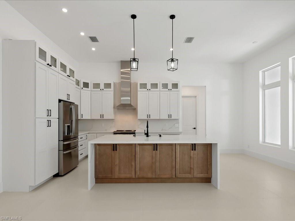 Kitchen with glass insert cabinets, stainless steel refrigerator with ice dispenser, light stone counters, a center island with sink, and recessed lighting