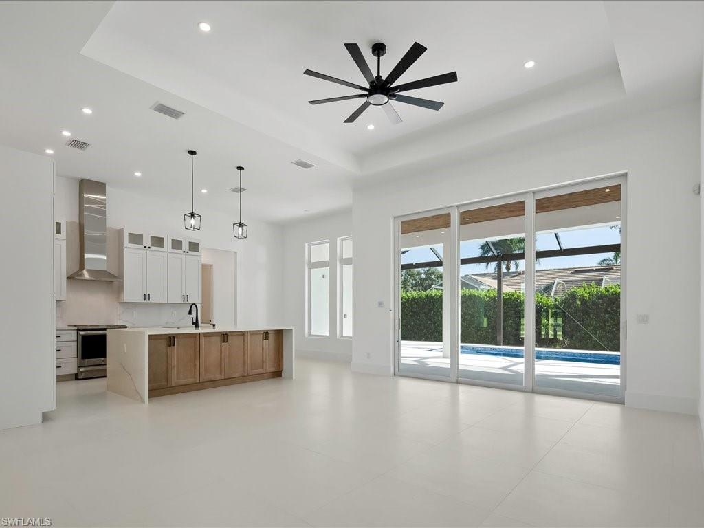 Kitchen with glass insert cabinets, white cabinets, a tray ceiling, stainless steel stove, and wall chimney exhaust hood