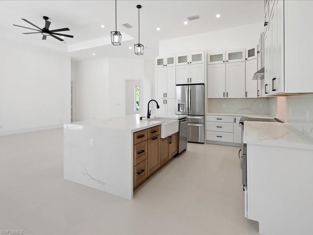 Kitchen with glass insert cabinets, light stone countertops, appliances with stainless steel finishes, hanging light fixtures, and white cabinets
