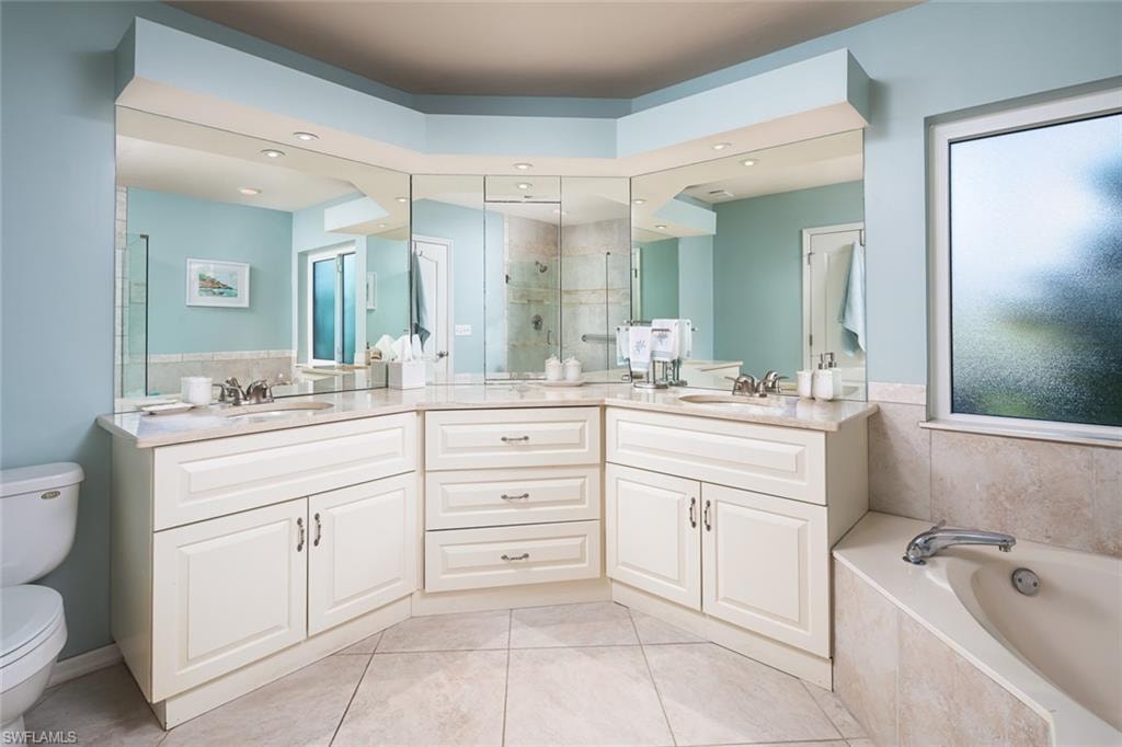 Full bathroom with a sink, a bath, toilet, a stall shower, and double vanity