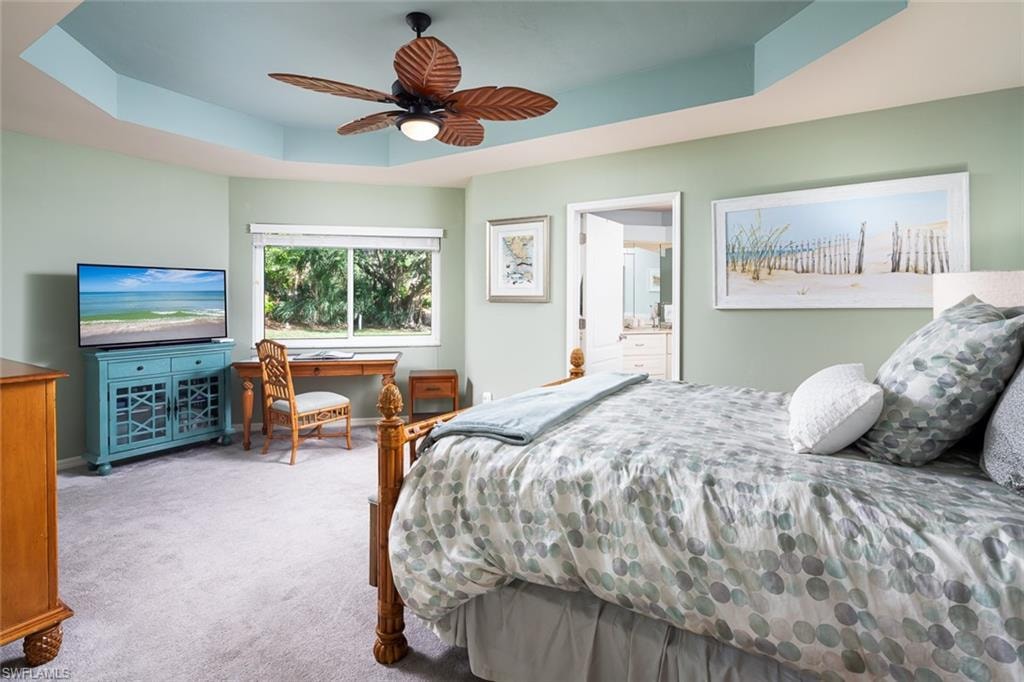 Carpeted bedroom featuring ensuite bathroom, a ceiling fan, a tray ceiling, and baseboards
