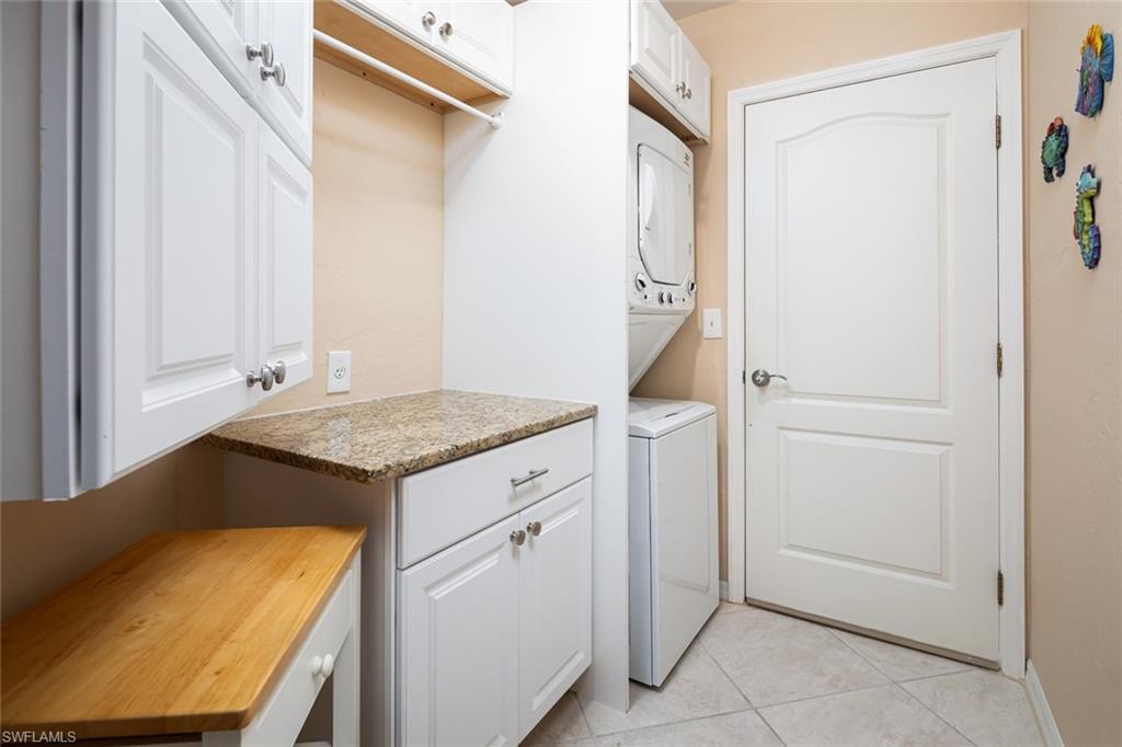 Washroom with light tile patterned floors, cabinet space, and stacked washer and clothes dryer