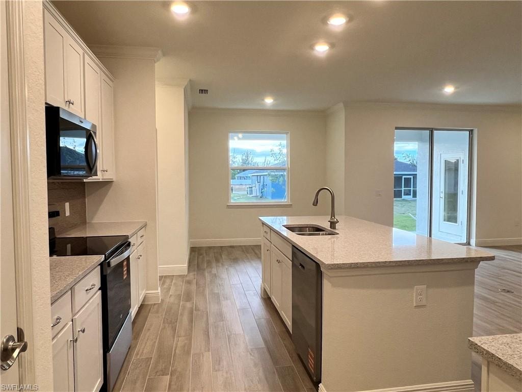 Kitchen with stainless steel appliances, light wood-type flooring, white cabinets, light stone counters, and recessed lighting