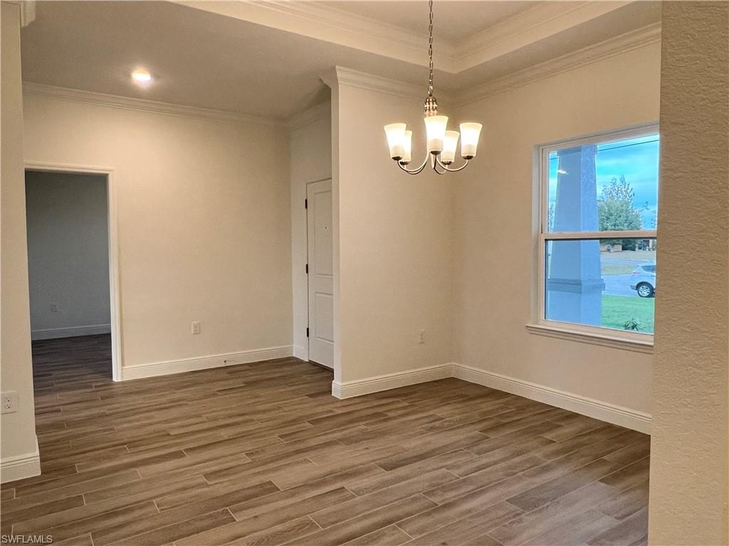 Empty room with wood finished floors, suspended lighting, and ornamental molding