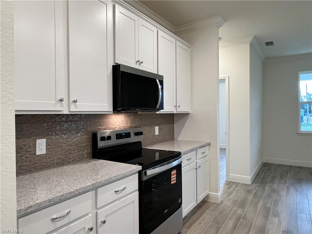 Kitchen with stainless steel appliances, light wood finished floors, crown molding, white cabinets, and light stone counters