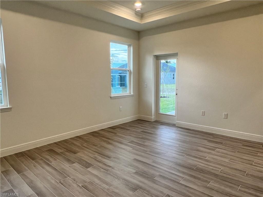 Empty room featuring ornamental molding, wood finish floors, and a raised ceiling