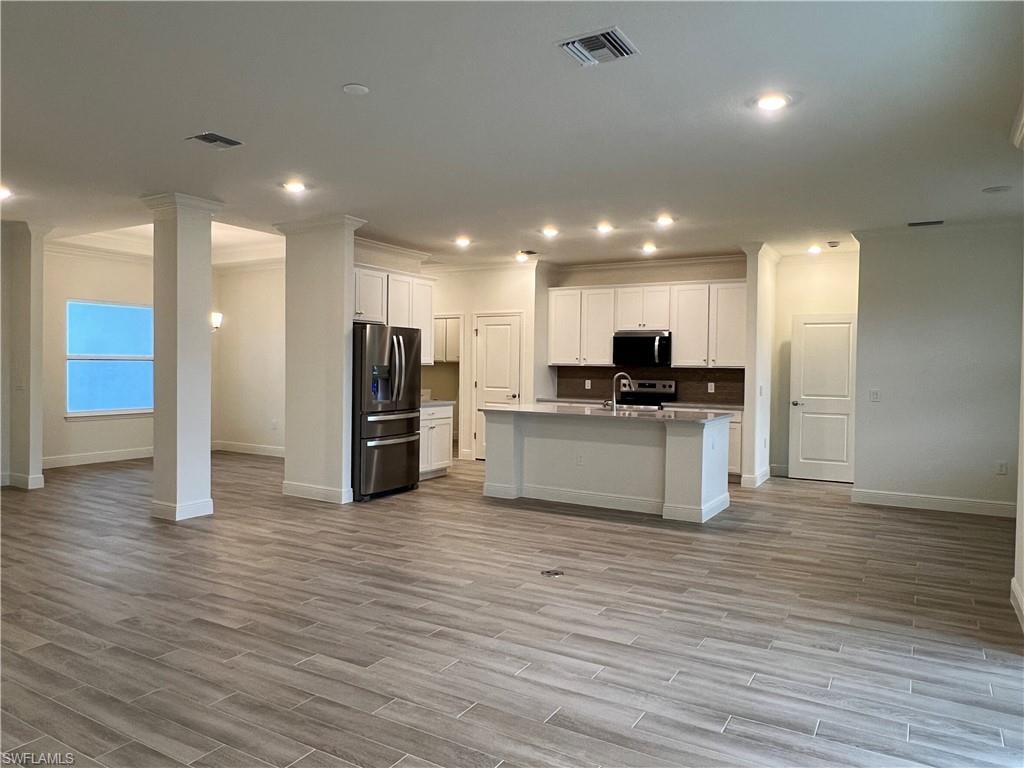 Kitchen featuring open floor plan, stainless steel appliances, white cabinets, a kitchen island with sink, and recessed lighting