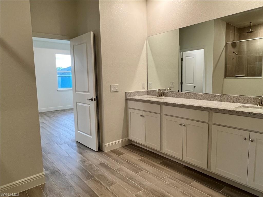 Bathroom featuring a textured wall, double vanity, wood tiled floors, and a tile shower
