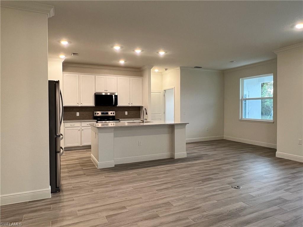 Kitchen featuring white cabinetry, stainless steel appliances, a center island with sink, recessed lighting, and light wood-type flooring