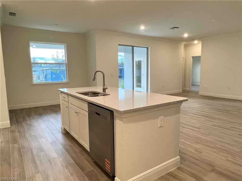 Kitchen featuring white cabinetry, light wood-type flooring, dishwasher, light stone counters, and crown molding