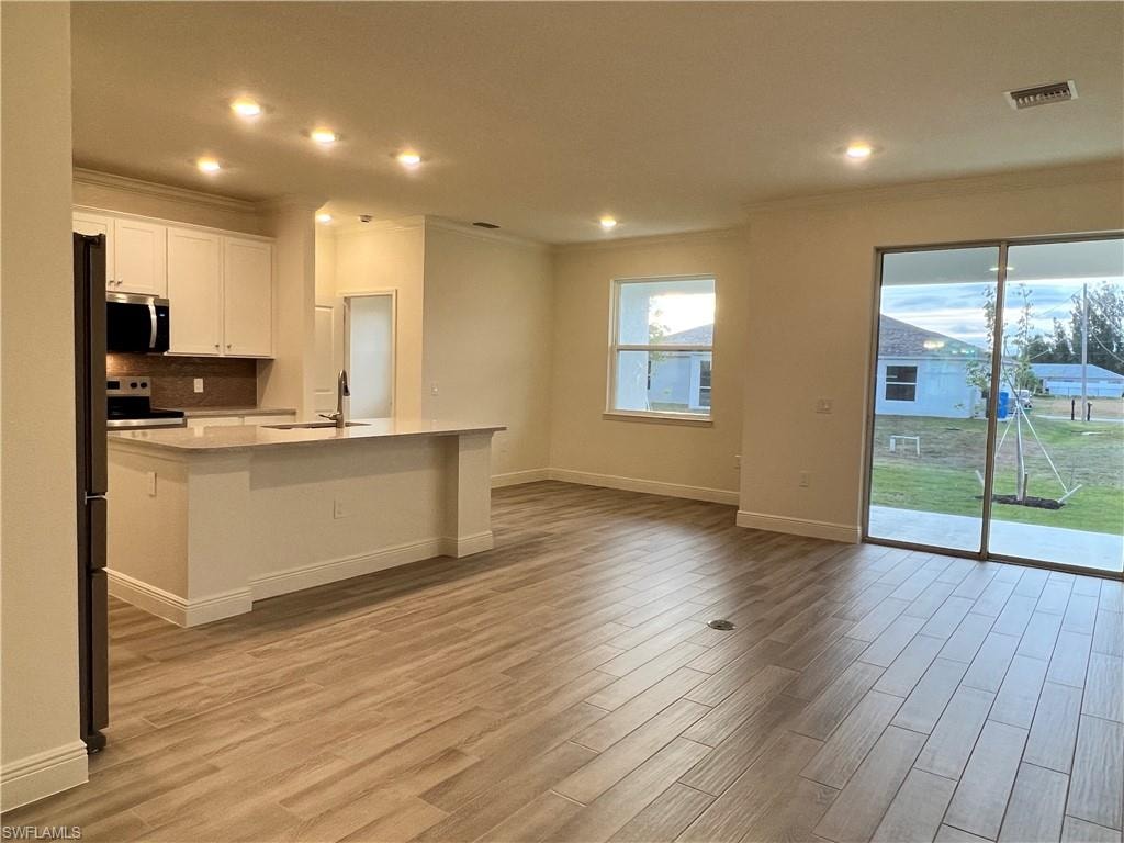 Kitchen with white cabinets, stainless steel appliances, an island with sink, recessed lighting, and light wood finished floors