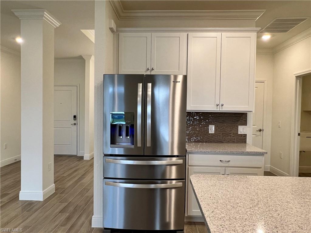 Kitchen with crown molding, stainless steel fridge, light stone counters, white cabinetry, and dark wood-style floors