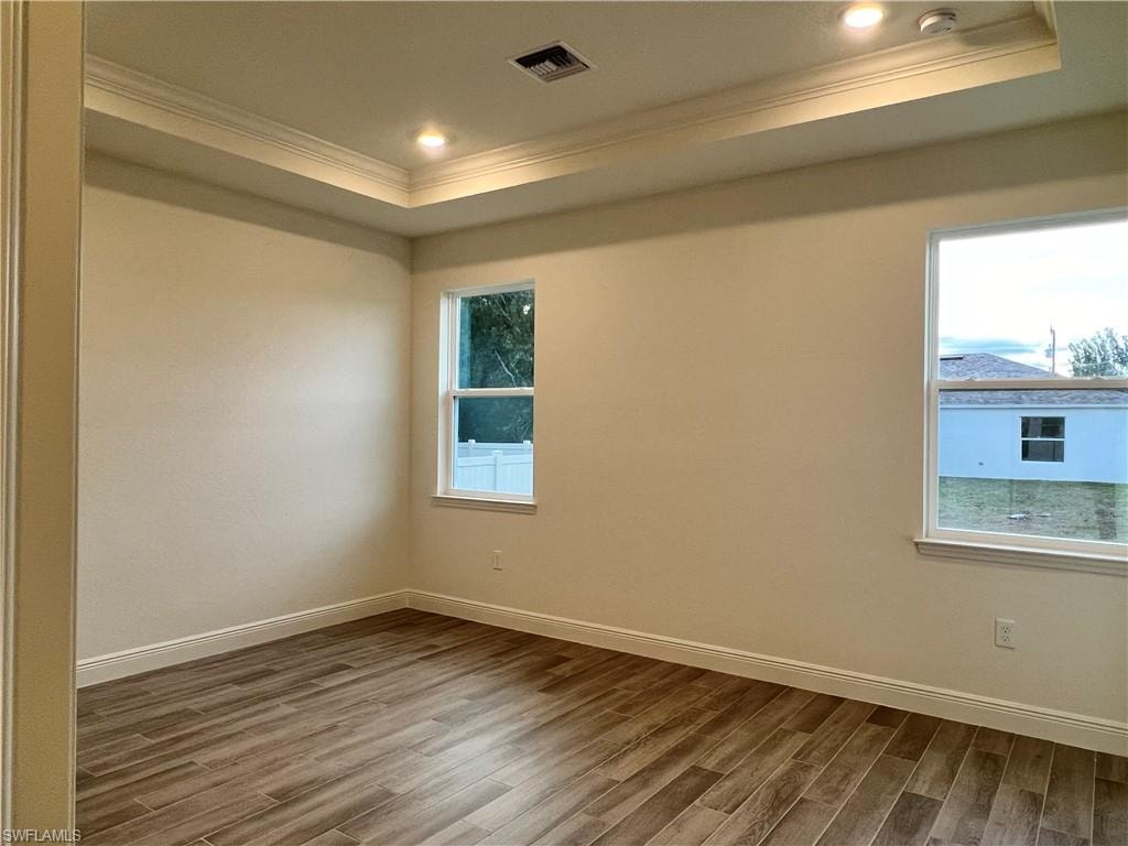 Spare room with wood finished floors, ornamental molding, a raised ceiling, and recessed lighting