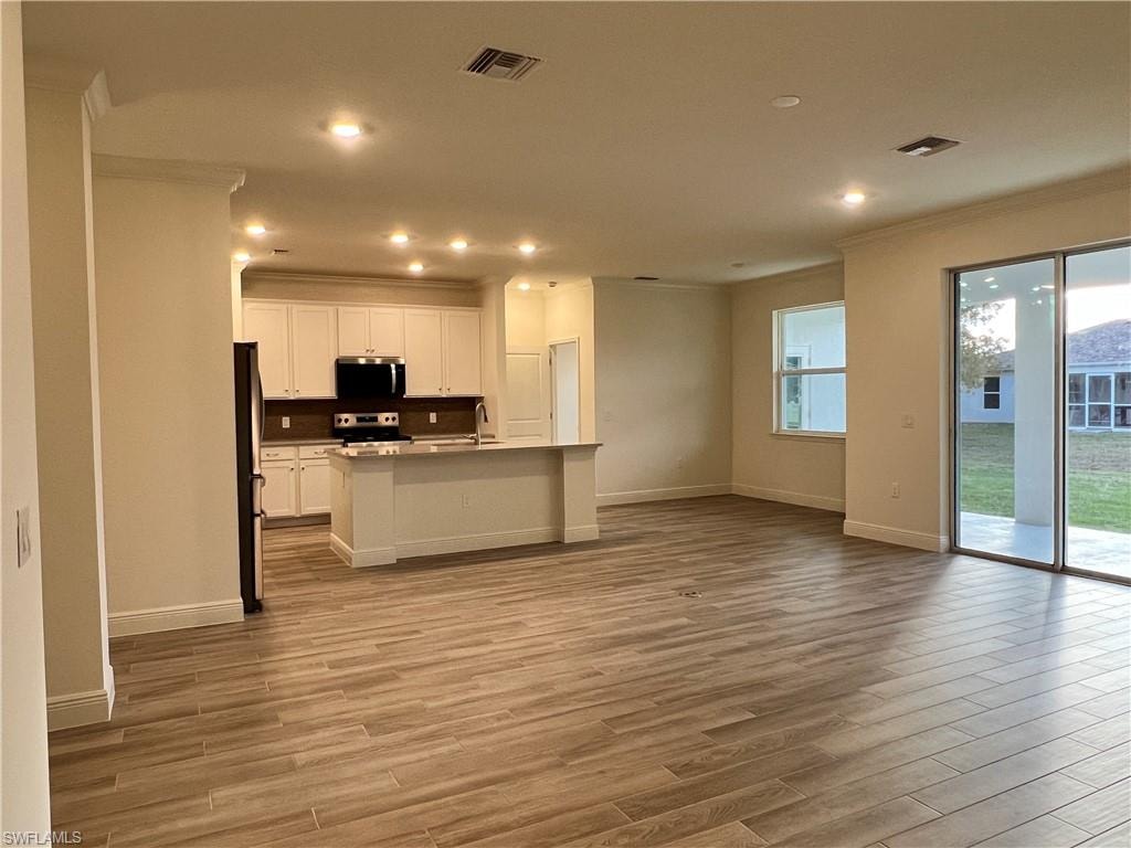 Kitchen with open floor plan, white cabinetry, a center island with sink, stainless steel appliances, and light wood-style floors
