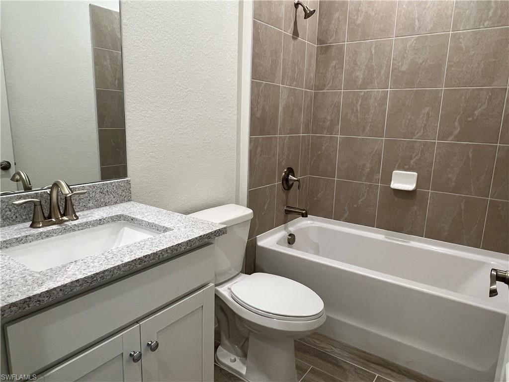 Bathroom featuring a textured wall, vanity, tub / shower combination, and wood finish floors