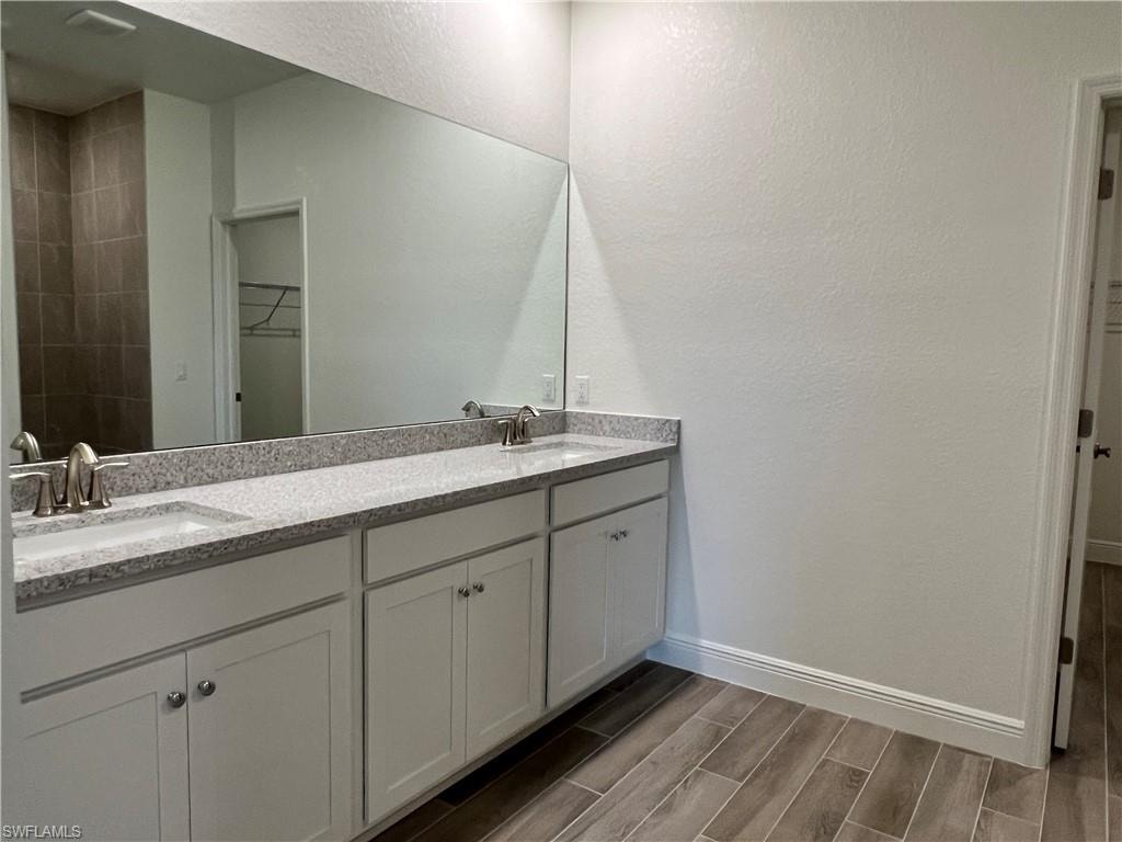 Full bath featuring a walk in closet, a textured wall, double vanity, and wood finish floors