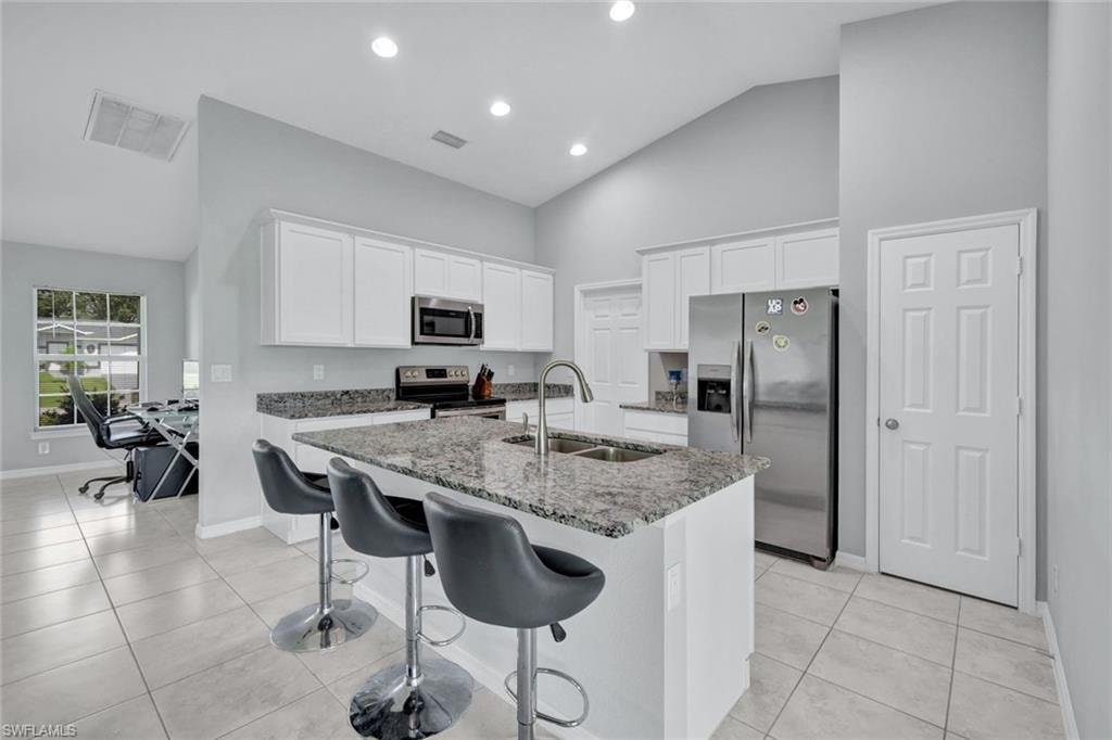 Kitchen with white cabinetry, appliances with stainless steel finishes, dark stone counters, a kitchen bar, and a kitchen island with sink