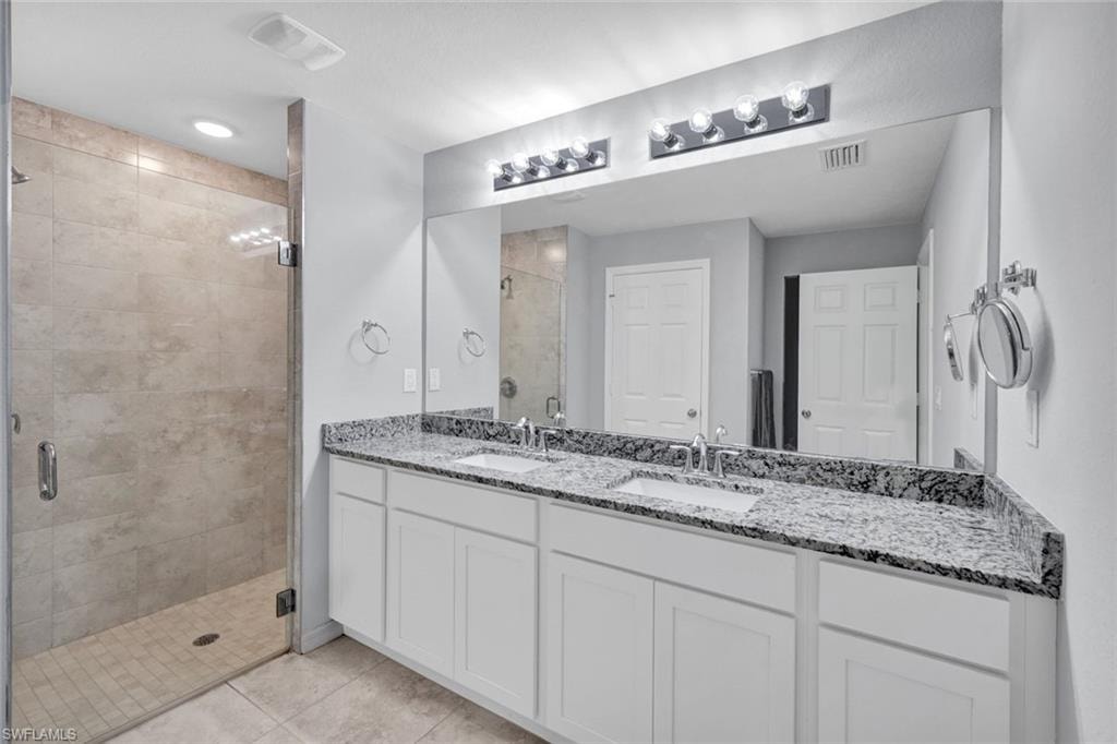 Bathroom featuring a stall shower, double vanity, and light tile patterned flooring