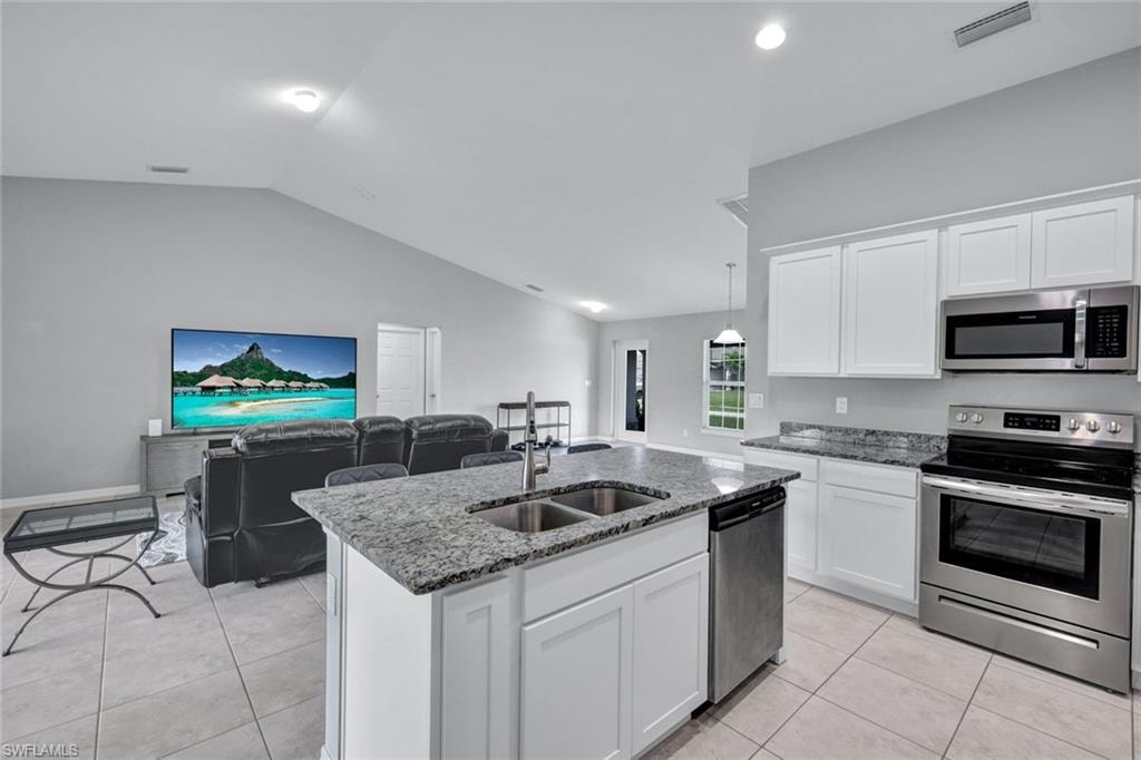 Kitchen featuring stainless steel appliances, white cabinetry, dark stone counters, open floor plan, and vaulted ceiling