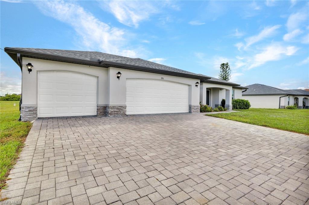 Ranch-style home with an attached garage, stone siding, a front yard, decorative driveway, and stucco siding