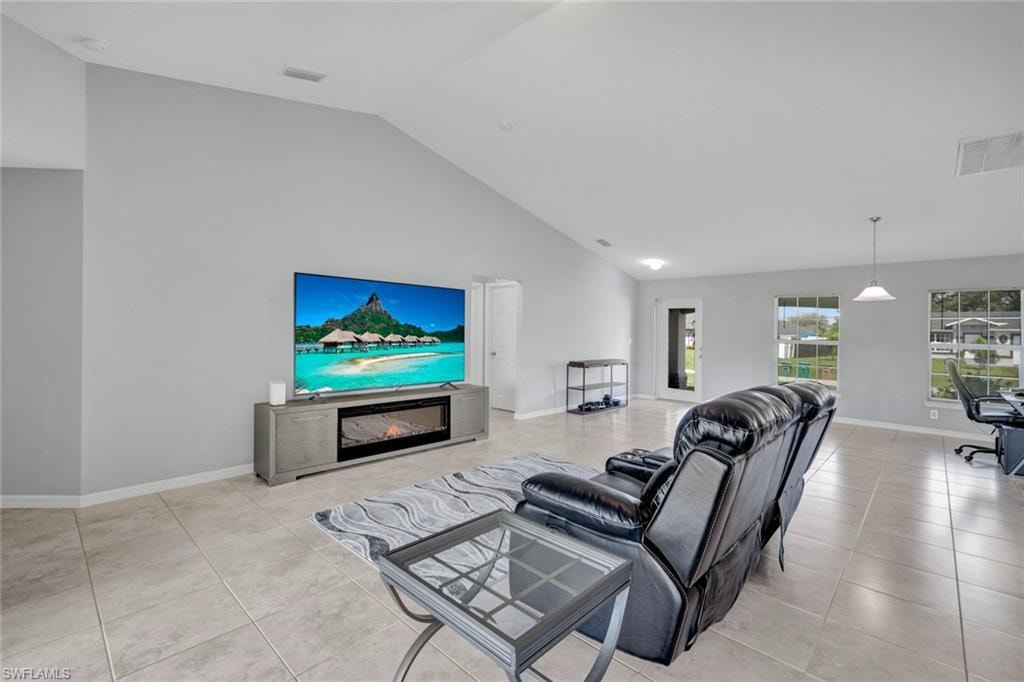 Living area featuring a glass covered fireplace, light tile patterned flooring, an office area, and high vaulted ceiling