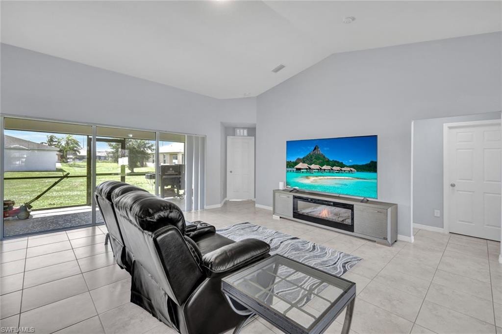 Living room featuring high vaulted ceiling, light tile patterned floors, and a glass covered fireplace