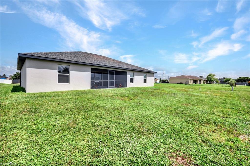 Rear view of house featuring a lawn, a sunroom, and stucco siding