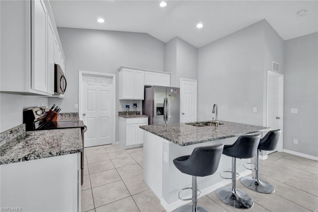 Kitchen with white cabinets, appliances with stainless steel finishes, a kitchen breakfast bar, light tile patterned flooring, and light stone countertops