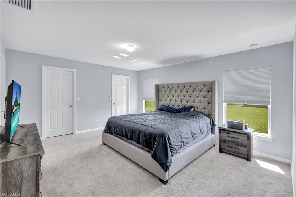 Bedroom featuring light colored carpet and multiple windows