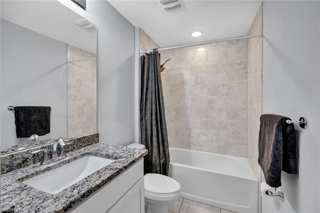 Bathroom with shower / bathtub combination with curtain, vanity, and light tile patterned floors