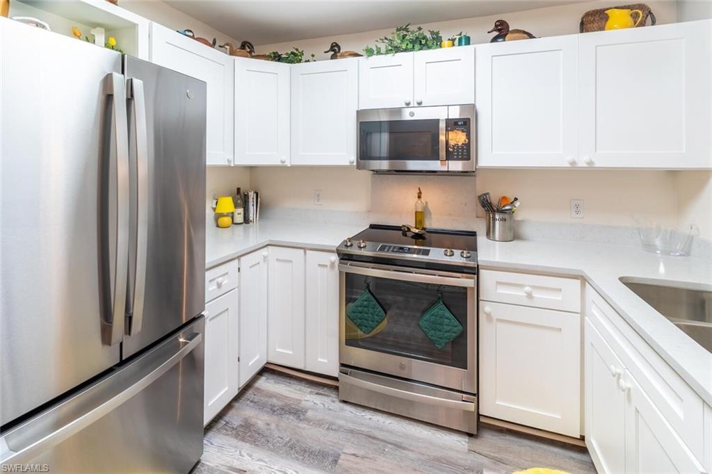 Kitchen with appliances with stainless steel finishes, white cabinets, light wood-type flooring, and light stone countertops