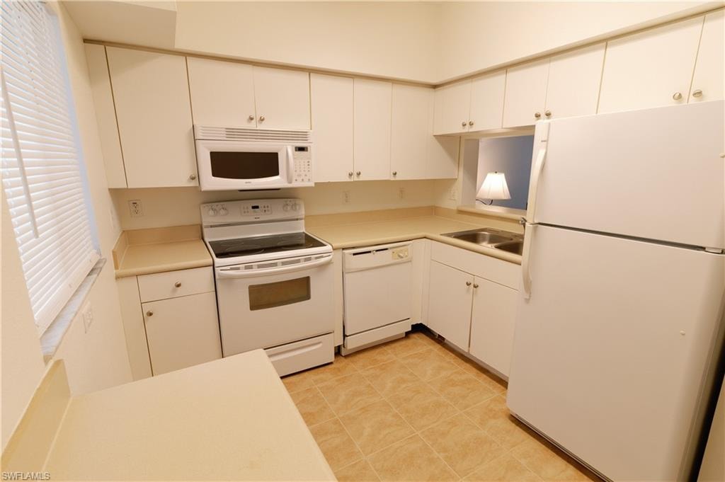 Kitchen with white appliances, light countertops, white cabinetry, and light tile patterned floors