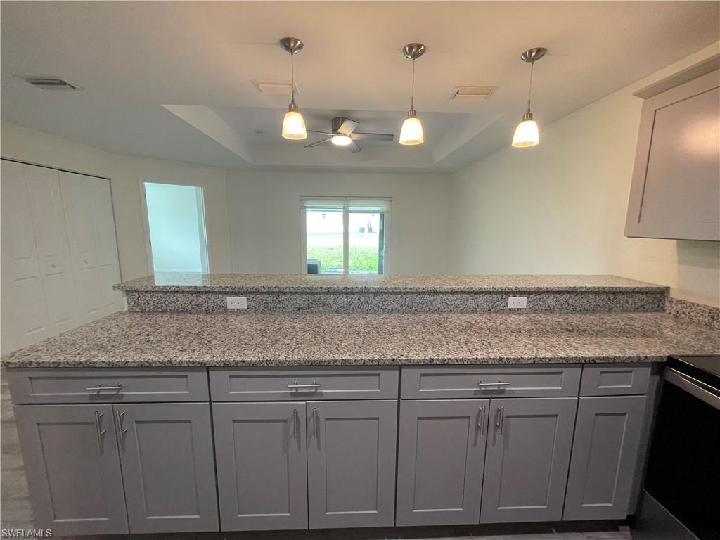 Kitchen with light stone counters, electric stove, decorative light fixtures, and gray cabinetry