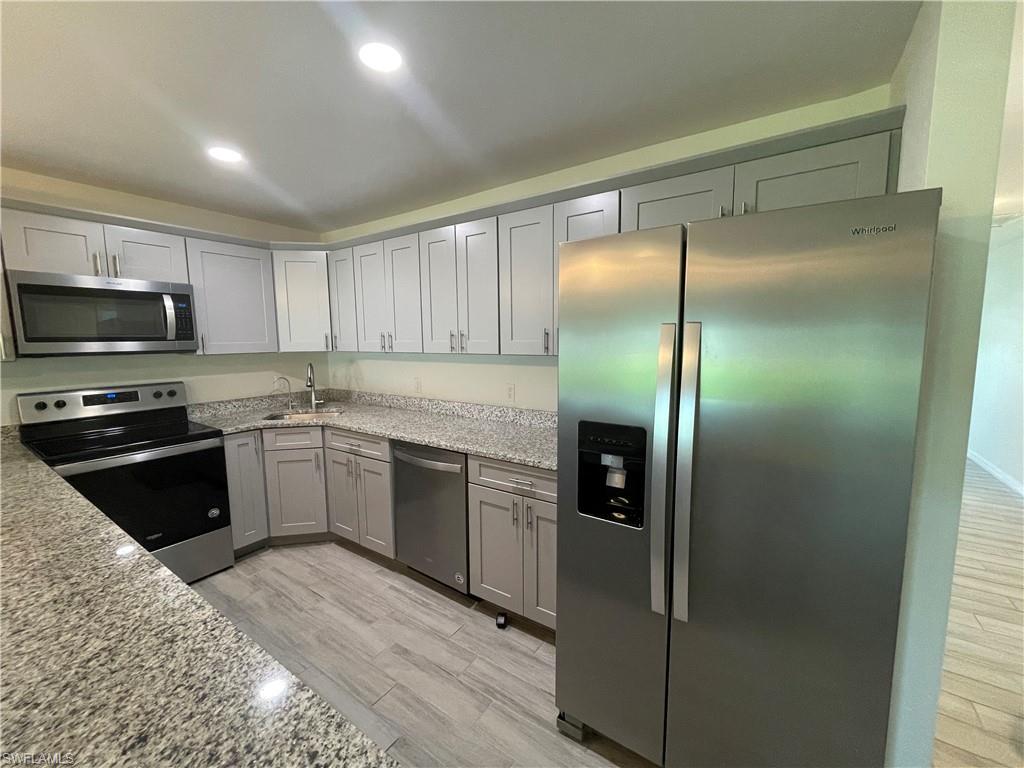 Kitchen featuring sink, stainless steel appliances, light wood-type flooring, and light stone countertops