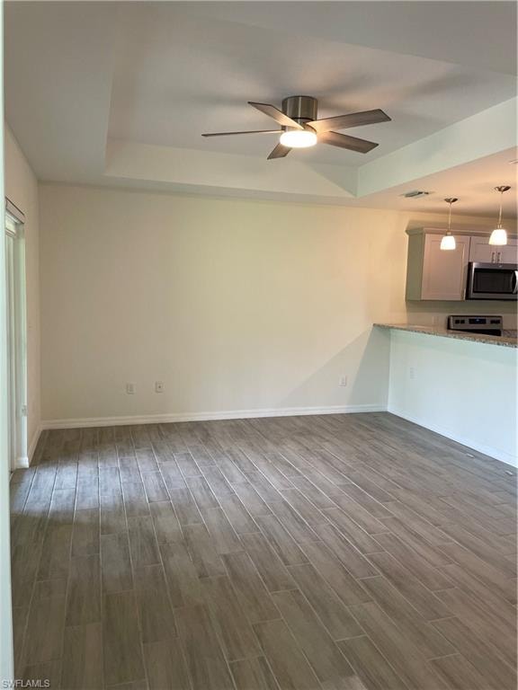 Unfurnished living room with ceiling fan, dark wood-type flooring, and a tray ceiling
