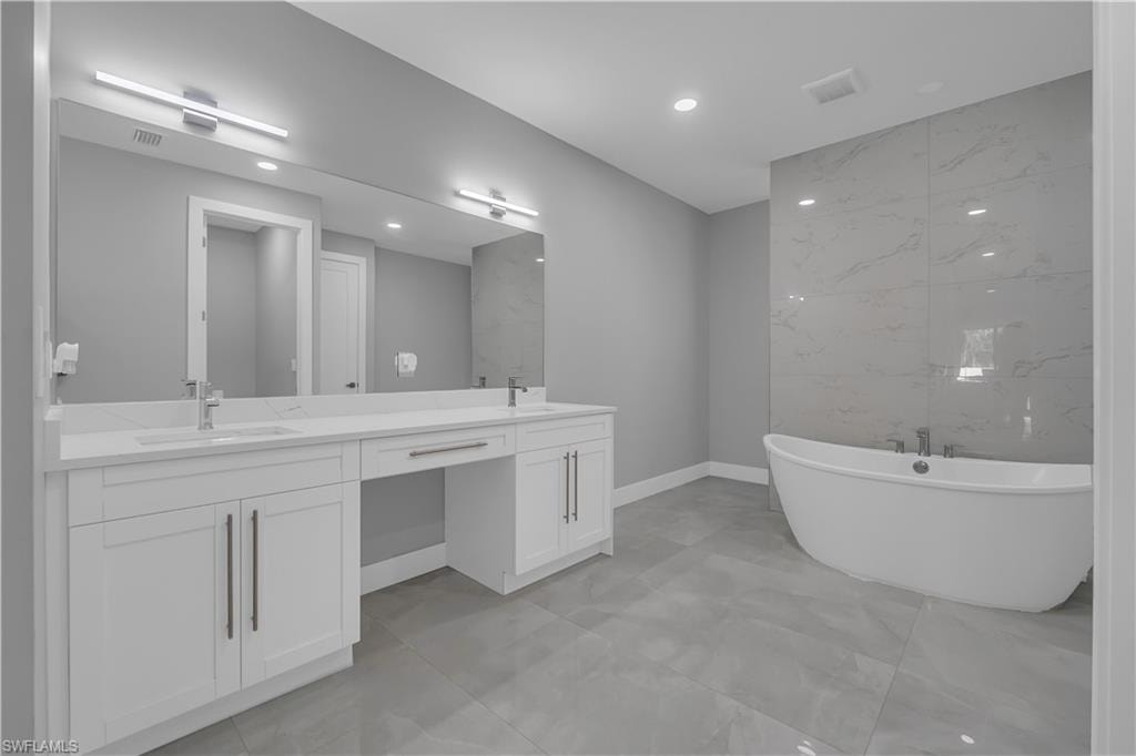 Full bathroom featuring double vanity, a freestanding tub, recessed lighting, and tile walls