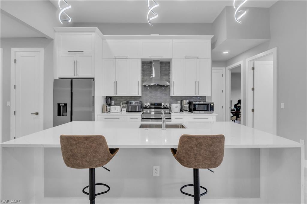 Kitchen with white cabinetry, appliances with stainless steel finishes, tasteful backsplash, wall chimney exhaust hood, and a spacious island