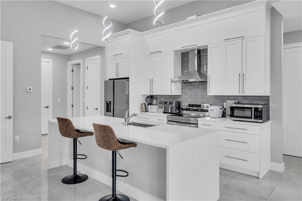 Kitchen with a kitchen bar, stainless steel appliances, wall chimney exhaust hood, white cabinets, and tasteful backsplash