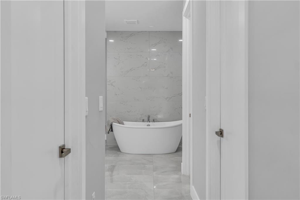 Bathroom with a freestanding tub, tile walls, and light marble finish flooring