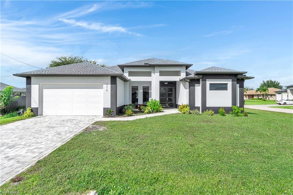 Prairie-style home with stucco siding, decorative driveway, a front yard, and an attached garage