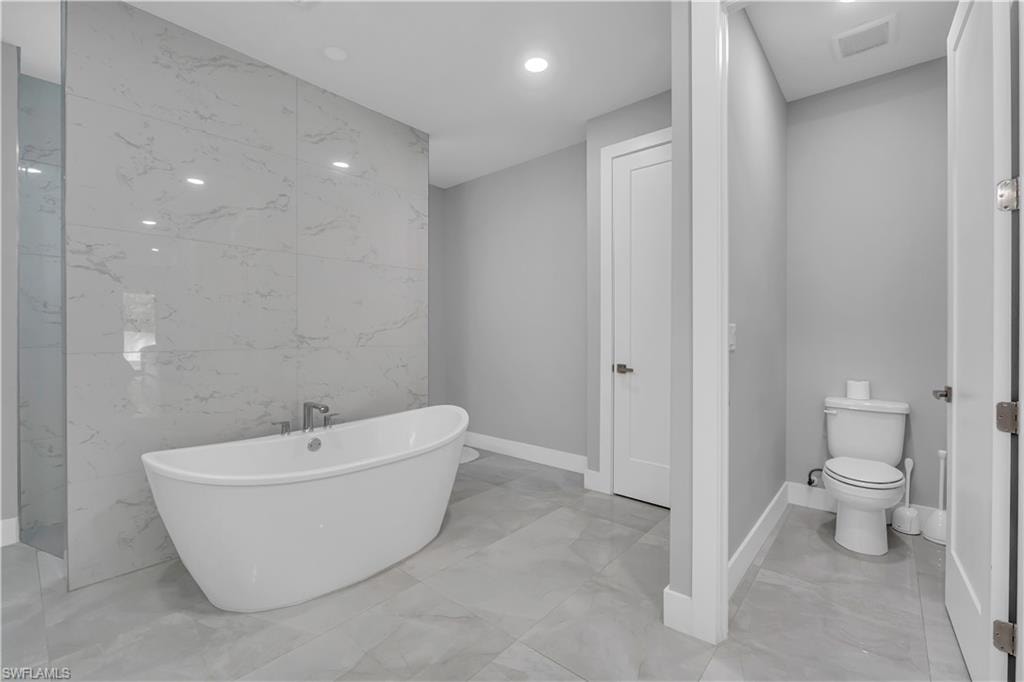 Bathroom featuring tile walls, a freestanding tub, light marble finish flooring, and recessed lighting