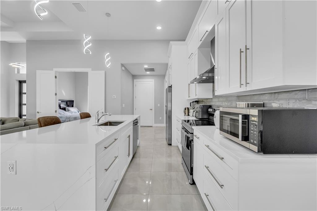 Kitchen featuring white cabinetry, stainless steel appliances, light stone countertops, open floor plan, and a spacious island